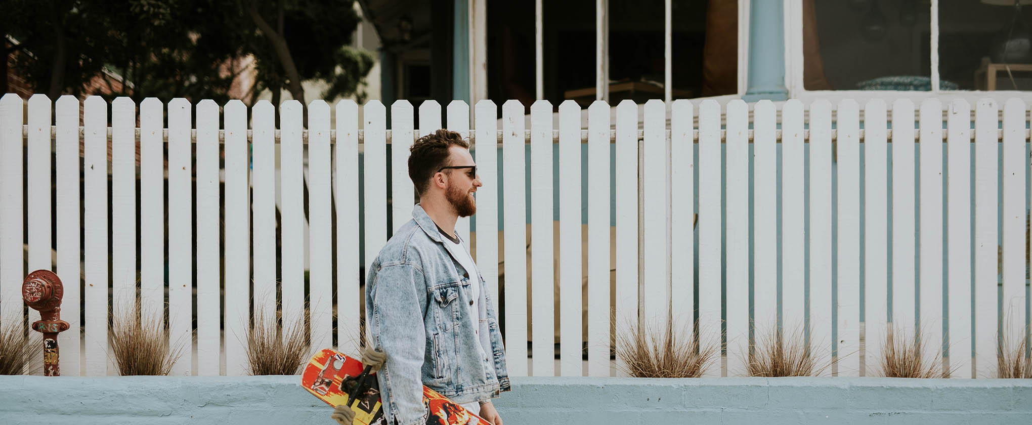 Person with jean jacket walking down street with colorful skateboard.