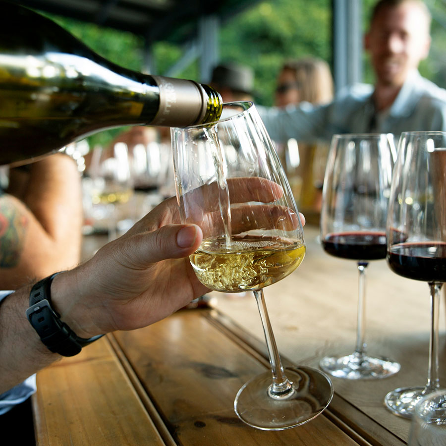 Person at wine bar pouring wine into wide glass.