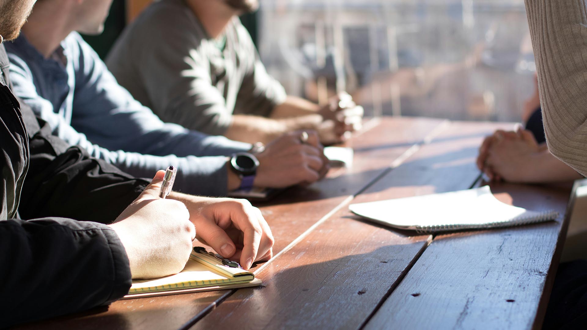 People working together at wood table with notepads and pens.
